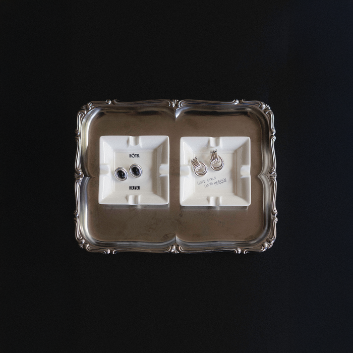 Silver tray with two white mini ashtrays that read: Hotel Heaven and Good Girls Go To Heaven, respectively.